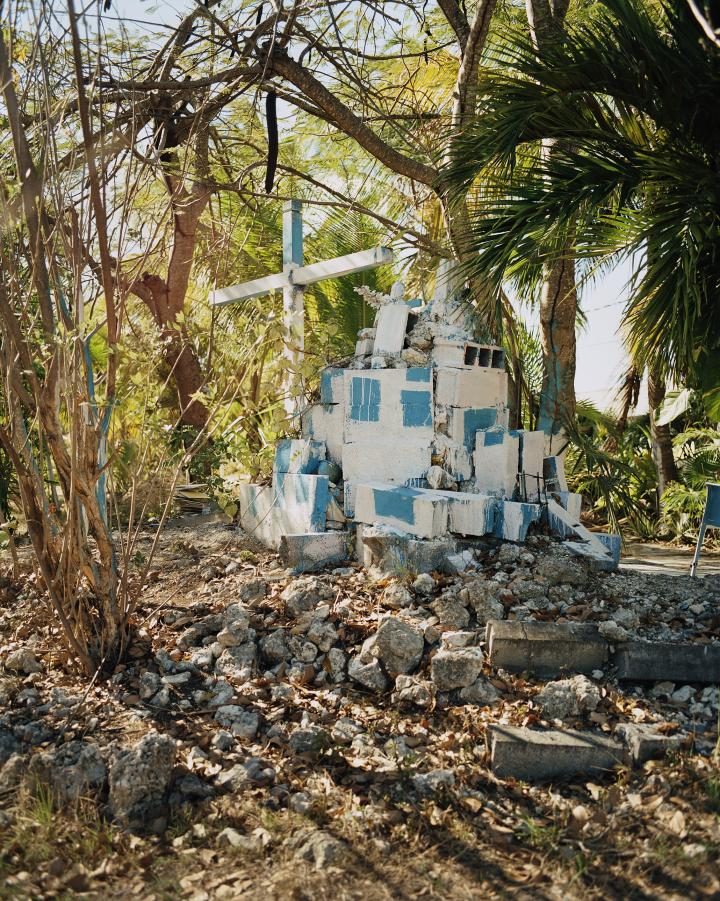 A blue and white man made building consisting of rubble with a cross in front of it.  