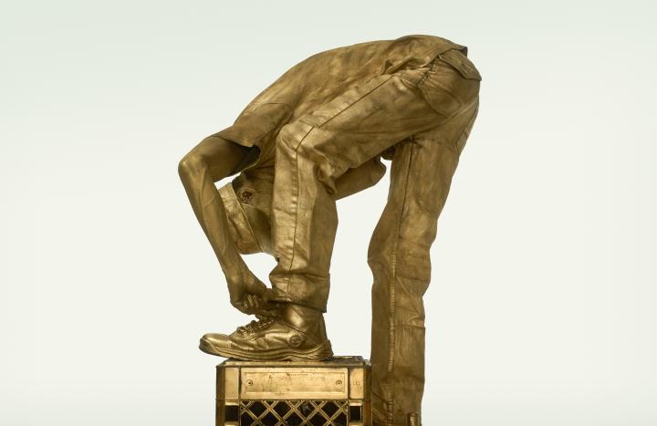 The image of gold man bending over to tie his shoes. 