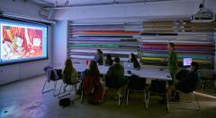 A group of students sitting at a round table watching a presentation on the projector. 