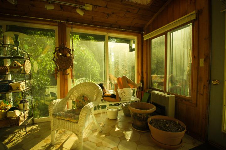 A woman splayed out and reading on a white bench in her sunroom.