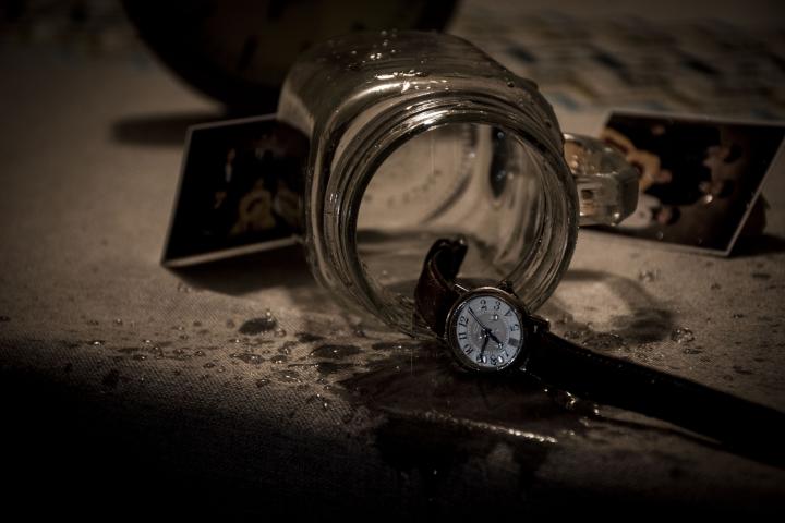 A mason jar on its side besides a dainty wrist watch and folded polaroids. 