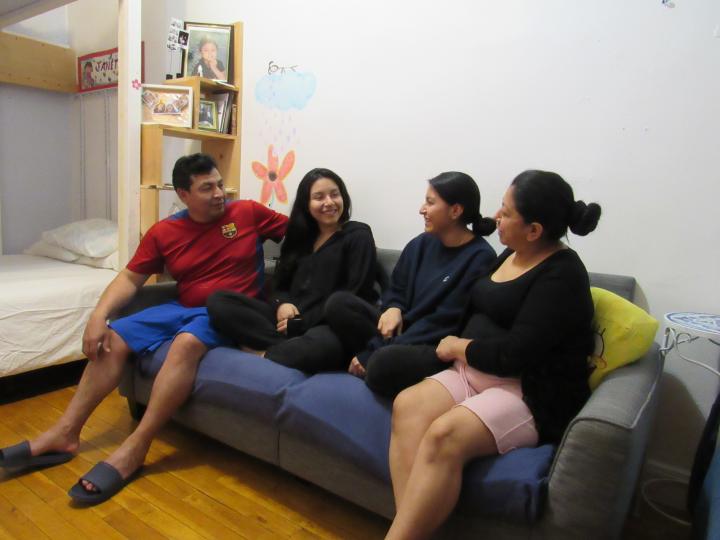 A family of four sitting on a couch, smiling and looking at one another. 