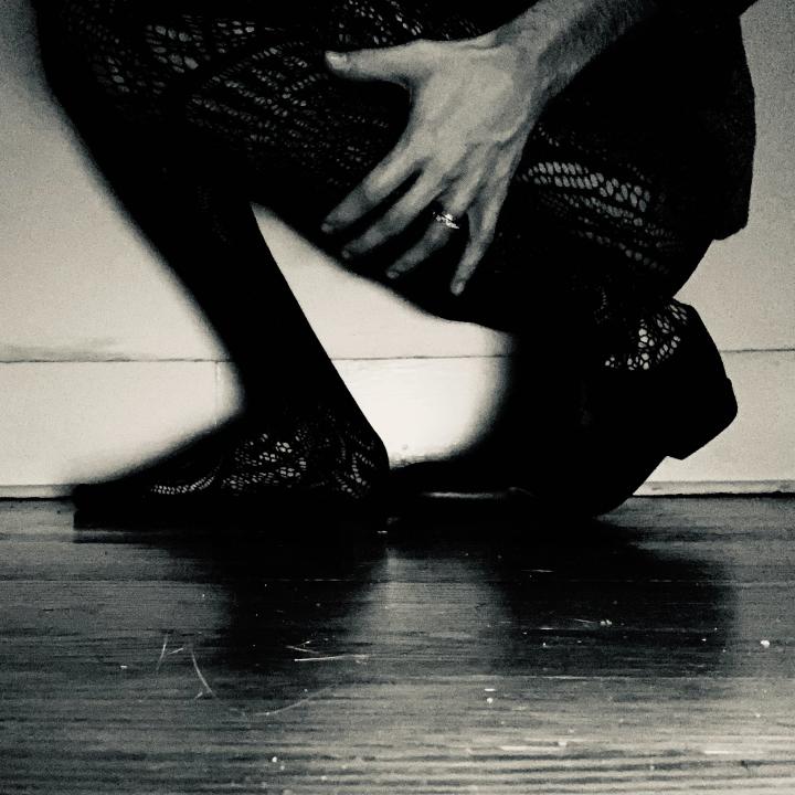 A beat up wooden floor and somebody squatting in black tights. 