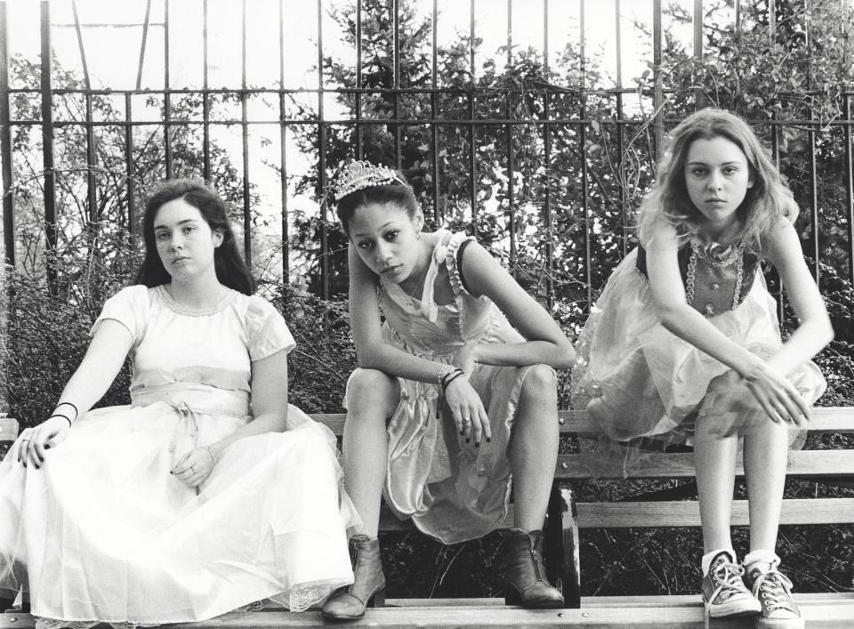 Black and white photo of three young women sitting on a bench wearing formal dresses